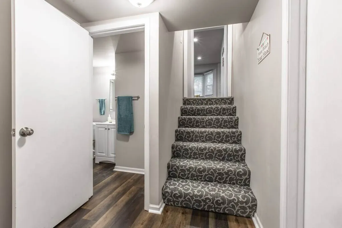 This image highlights a well-lit staircase near the bathroom door, complete with a mirror and towels. The composition evokes movement and the transition between different areas of the home, suggesting ongoing exploration and discovery even within the space.