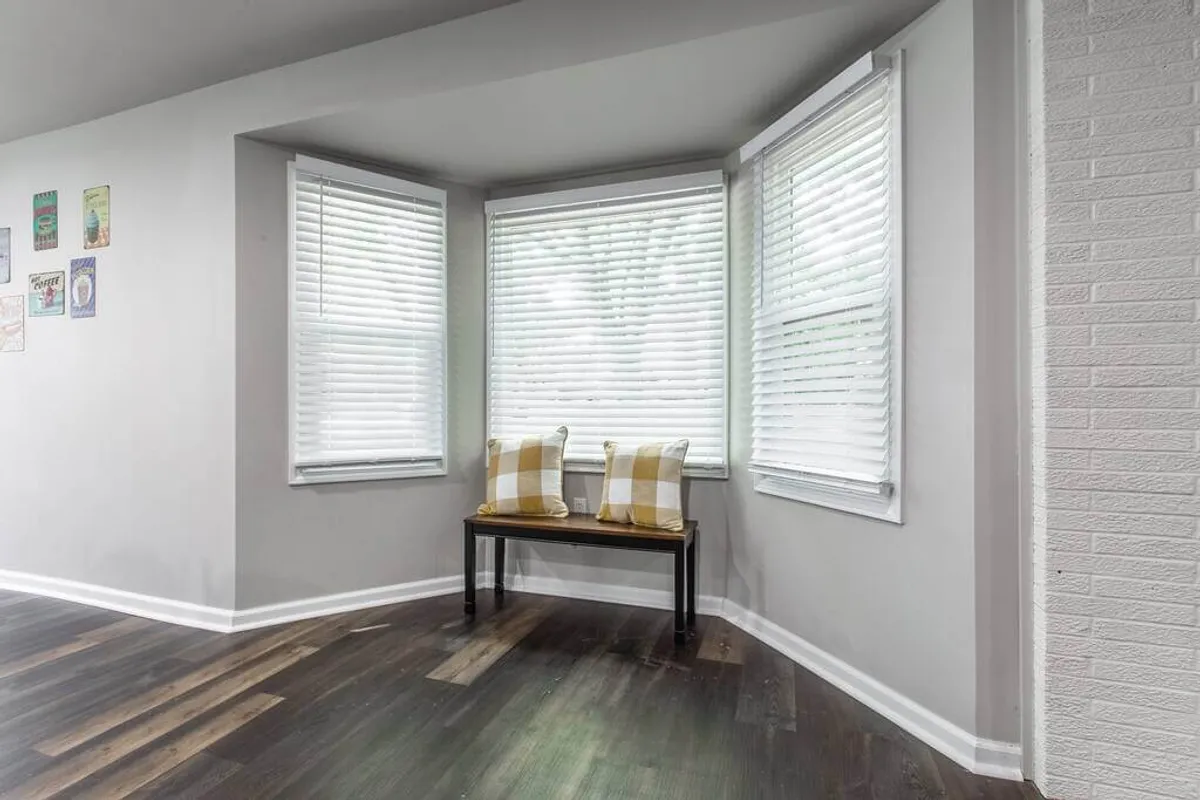 A cozy bay window seating area with decorative pillows and a wooden bench, bathed in natural light. The space invites relaxation, reading, or enjoying a quiet moment with a cup of coffee, creating a tranquil nook within the home.