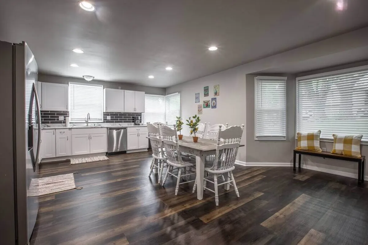 A cozy kitchen dining area with a welcoming table, surrounded by cabinetry and windows that fill the space with natural light. Artistic wall decor and comfortable seating create an ideal setting for family meals, coffee breaks, or planning outings.