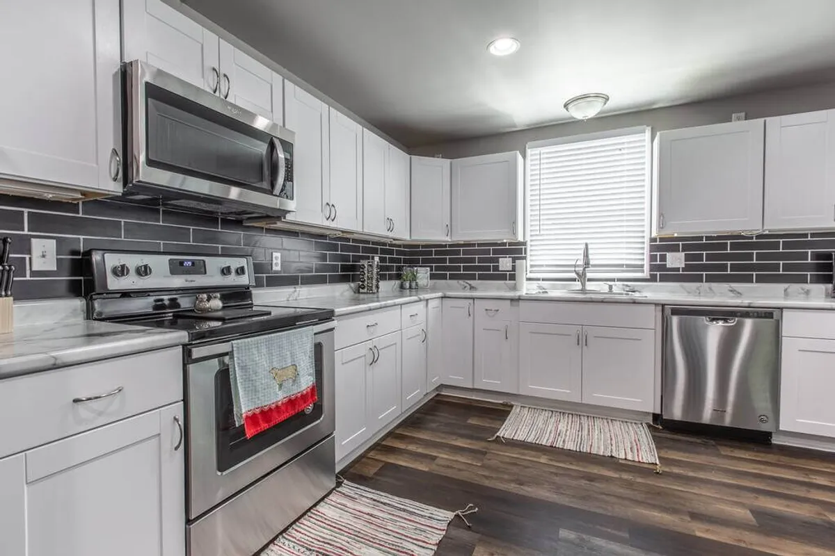 A bright, inviting kitchen with stainless steel appliances, sleek white cabinetry, a bold black backsplash, and expansive marble countertops. The space is perfectly organized for collaborative cooking and includes ample counter area for meal prep or entertaining.