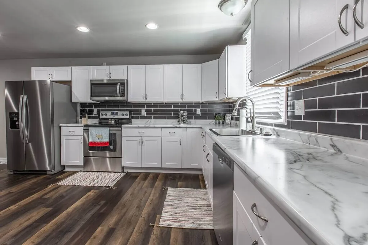 A stylish kitchen scene showcasing stainless steel appliances, a pristine marble countertop, and bright white cabinetry. The space is well-lit and clearly designed for both function and comfort, inviting both meal prep and socializing.