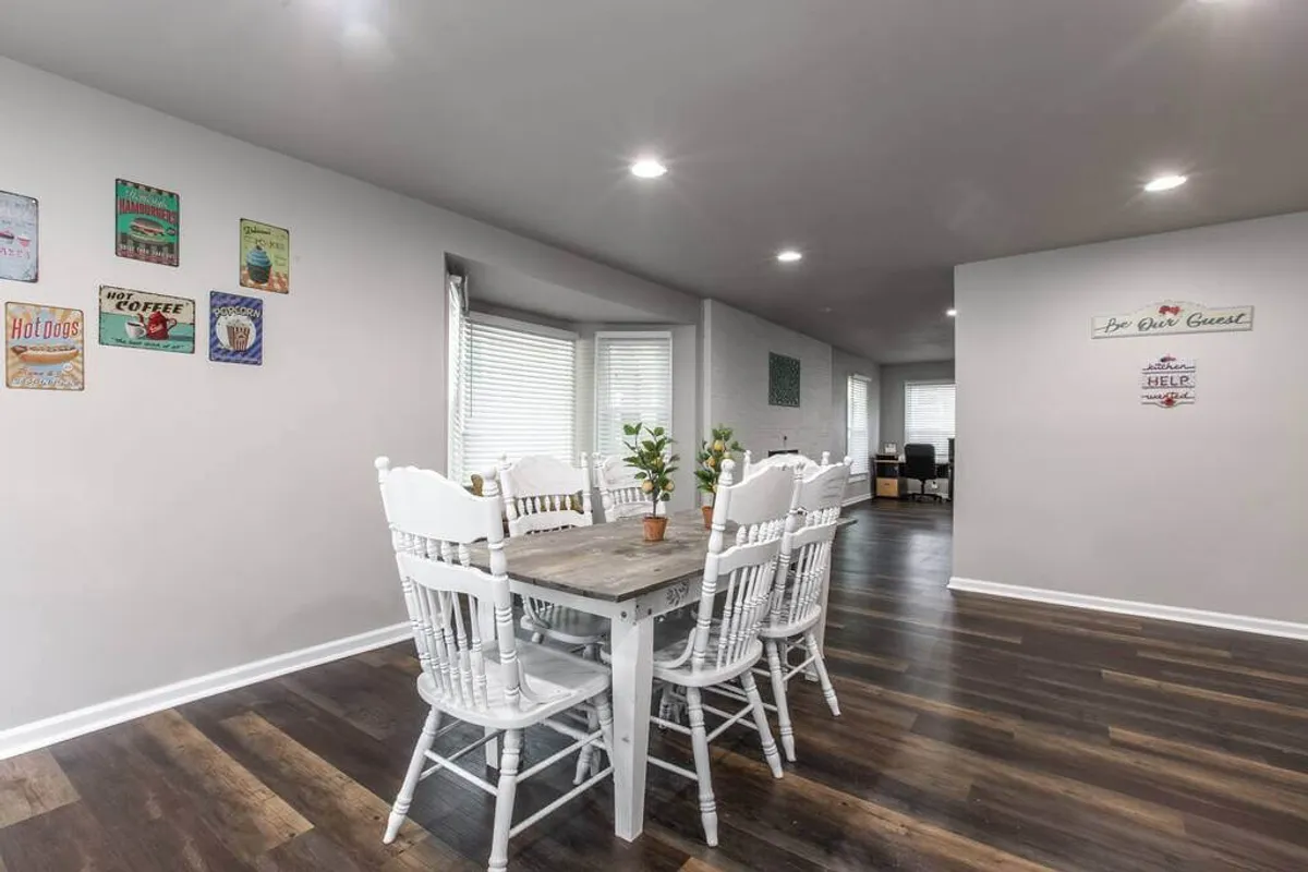 A bright, welcoming dining area featuring a large dining table surrounded by white chairs, with tasteful wall decorations that add warmth. The space feels ready for family meals or group celebrations, highlighting the home's capacity for hosting.