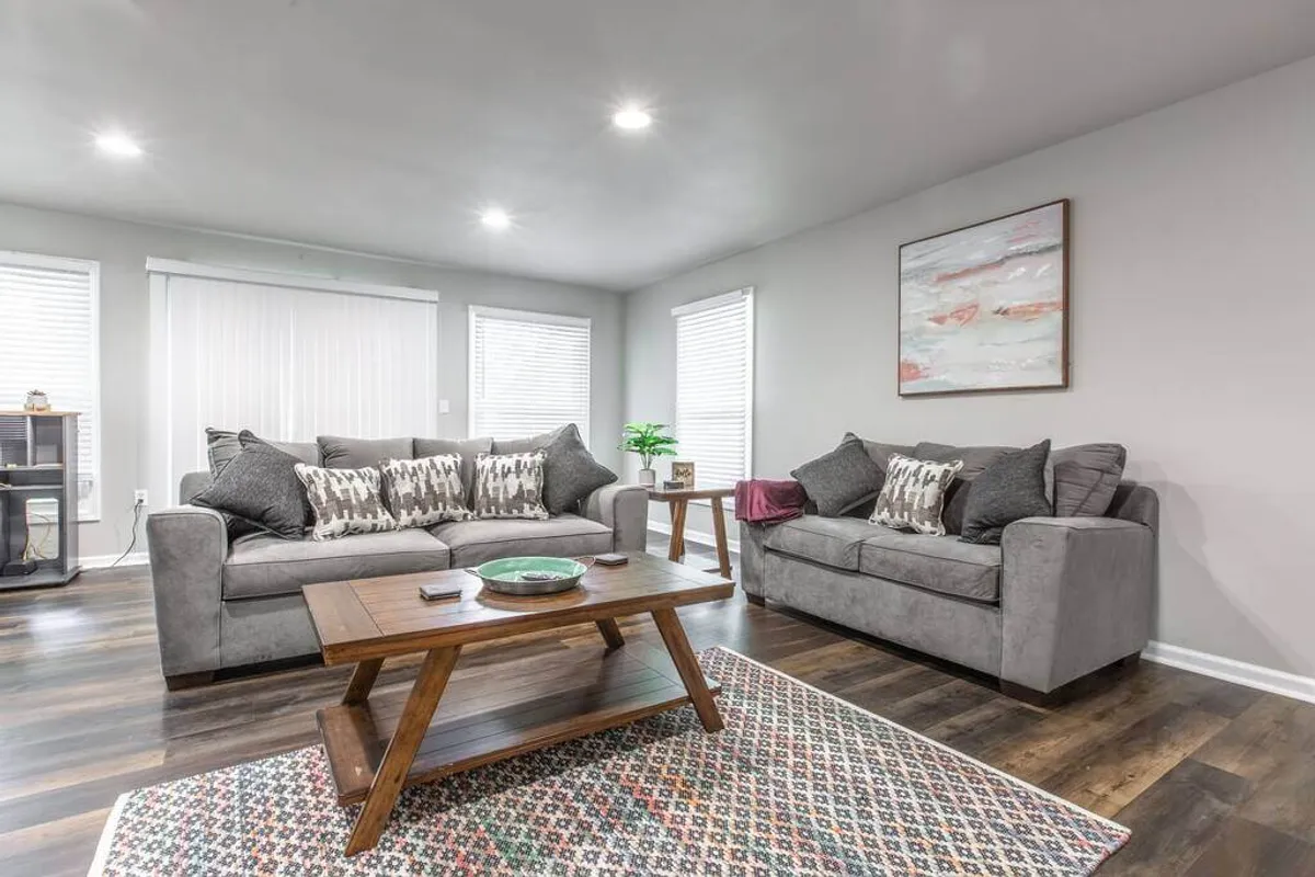 A cozy and inviting lounge area with comfortable sofas, a coffee table at the center, decorative pillows, and stylish artwork on the wall. The layout is designed for socializing, game playing, or relaxing with friends and family.